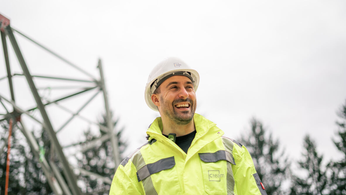 Ein Cteam Mitarbeiter lächelt neben einer Hochspannungsleitung, symbolisierend Energieprojekte.