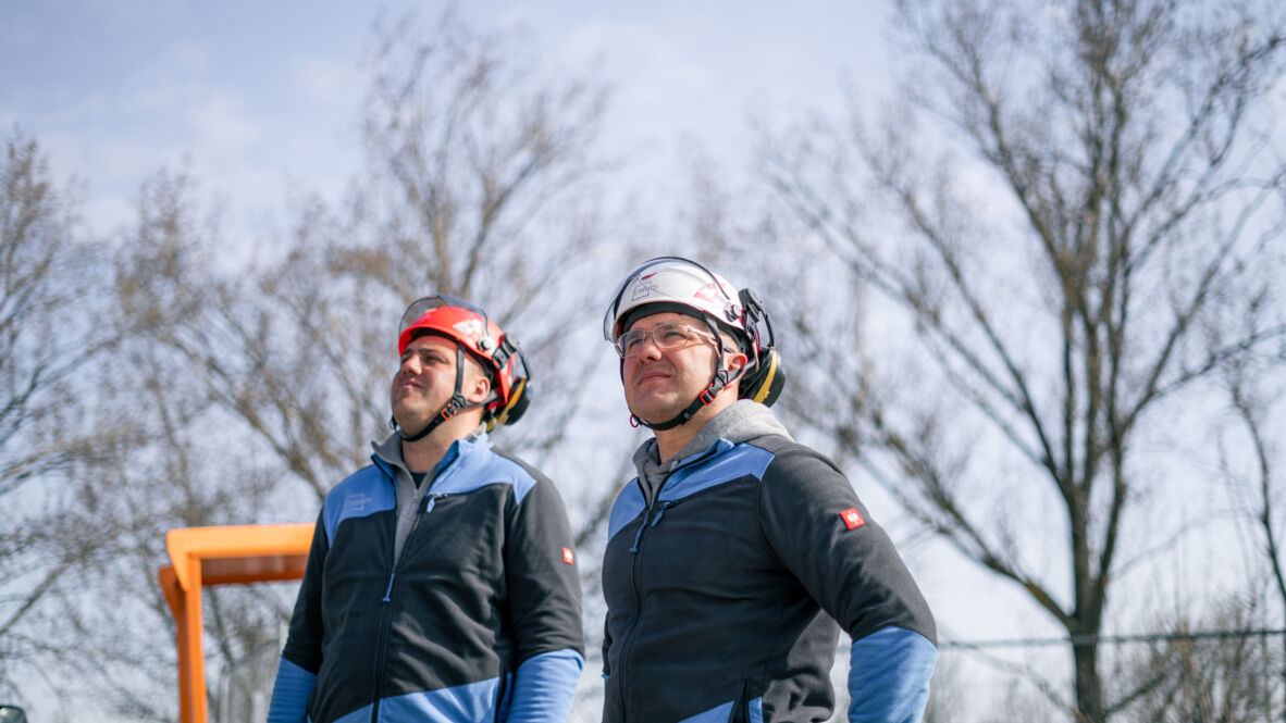 Two Cteam workers in safety helmets looking up, assessing overhead line construction. Two Cteam workers in safety helmets looking up, assessing overhead line construction.