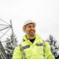 Ein Cteam Mitarbeiter l&auml;chelt neben einer Hochspannungsleitung, symbolisierend Energieprojekte.