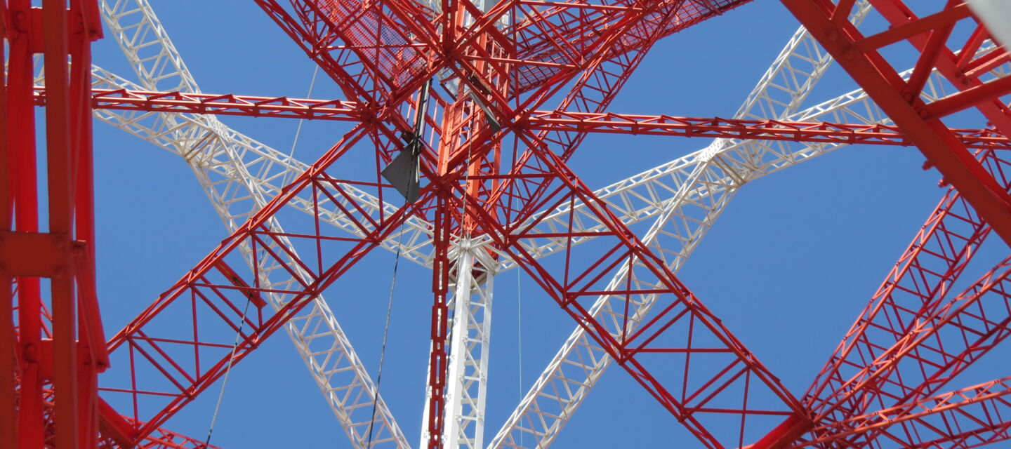 Blick in die Stahlkonstruktion eines rot-weißen Mastes. Beispiel für Mastbau-Projekte von Cteam.