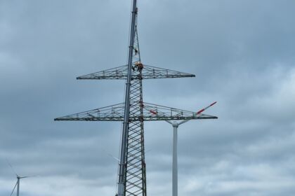 Freileitungsbau durch Cteam: Montagearbeiten an einem Gittermast nahe Windkraftanlagen.