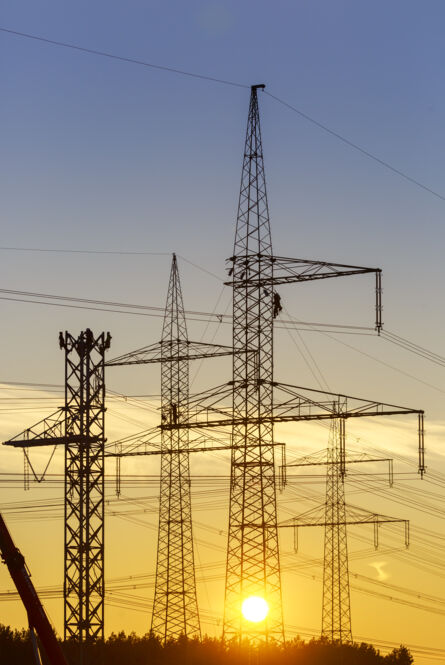 Stromleitungen und Freileitungsmasten im Sonnenuntergang mit Monteuren bei Arbeiten an der Leitung.