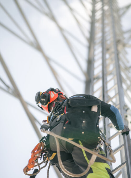Cteam worker in safety gear climbing infrastructure tower for assembly or maintenance. Cteam worker in safety gear climbing infrastructure tower for assembly or maintenance.